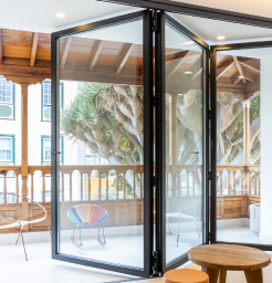 A picture of Cobalt Aluminium's black door product called Bi-Fold Plus. It shows it seperating the environment and unifying the houses space.